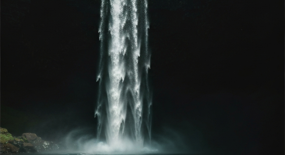 A tall waterfall falling into a dark pool, lit by a single hard shaft of light, deep shadow all around