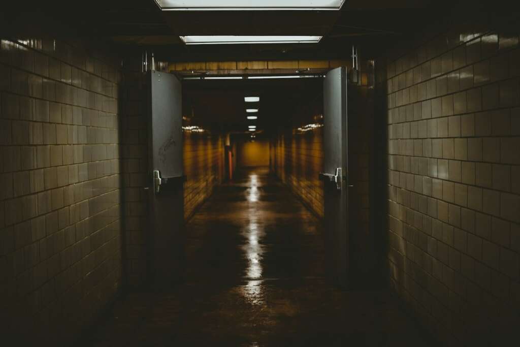 Home 7 A dark tiled corridor with open double doors leading into a dim passage lit by a single strip of light