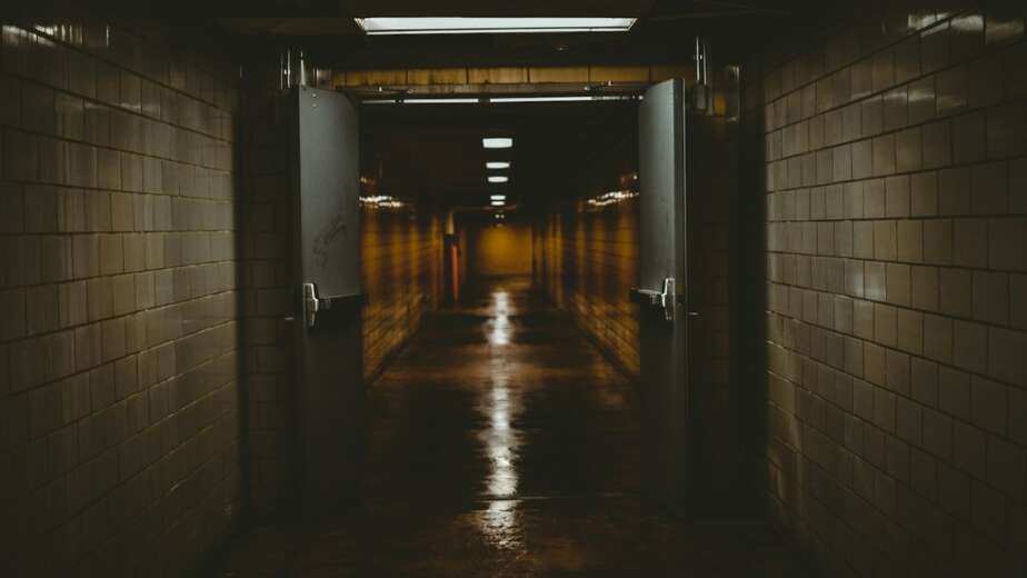 A dark tiled corridor with open double doors leading into a dim passage lit by a single strip of light