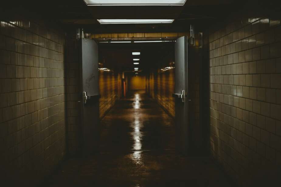 A dark tiled corridor with open double doors leading into a dim passage lit by a single strip of light